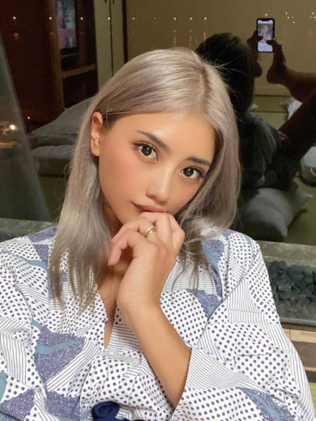 Young woman with silver hair in a polka dot shirt, resting her chin on her hand.