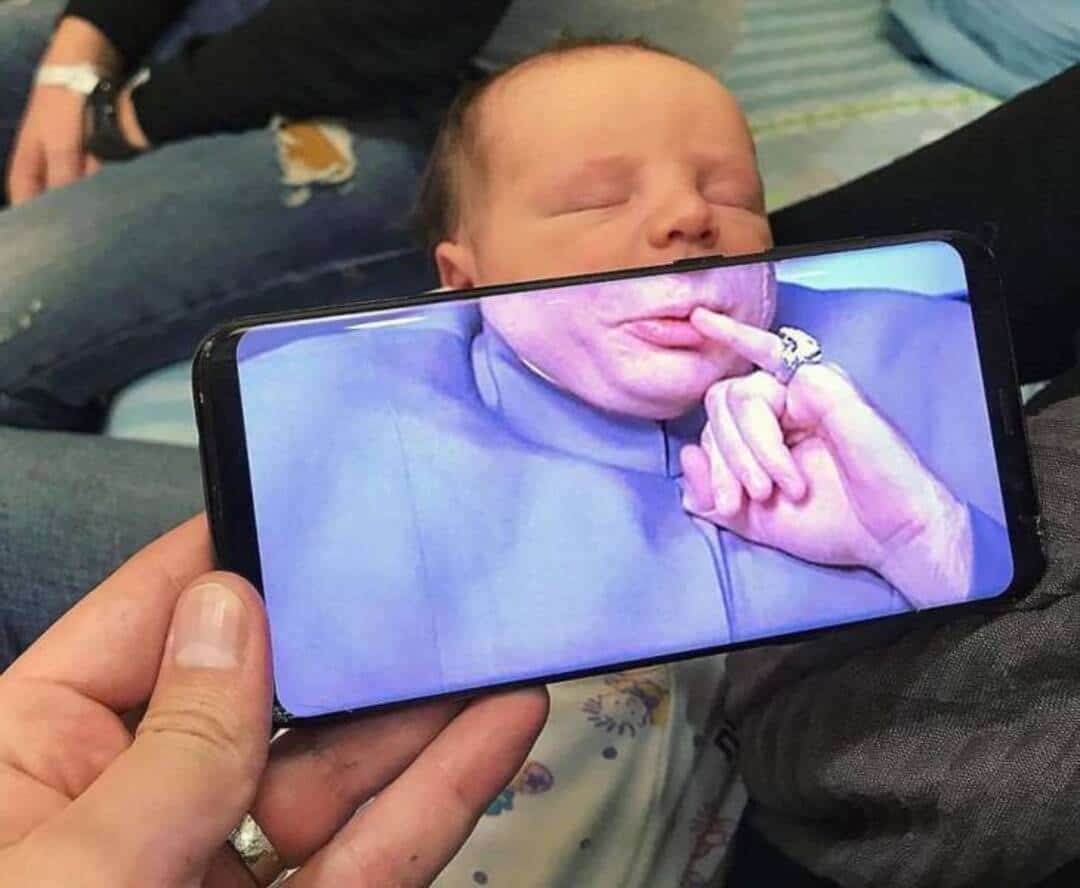 Baby with face pressed against phone screen, making a funny face.