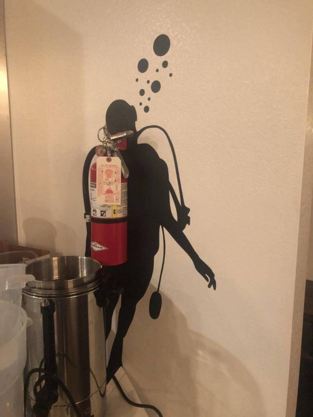 Fire extinguisher with a silhouette of a diver and bubbles on the wall.
