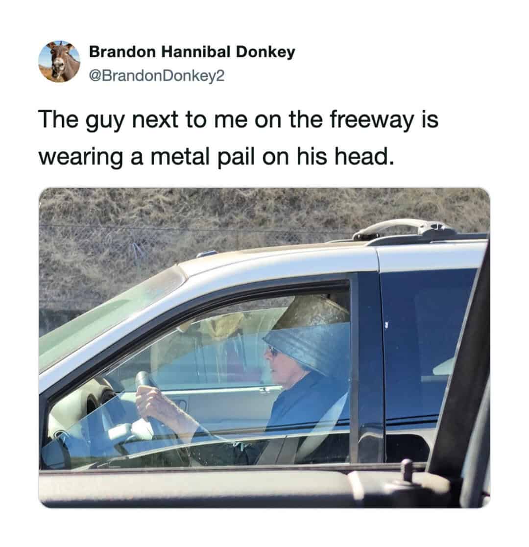 Man wearing a metal pail on his head while driving on the freeway.