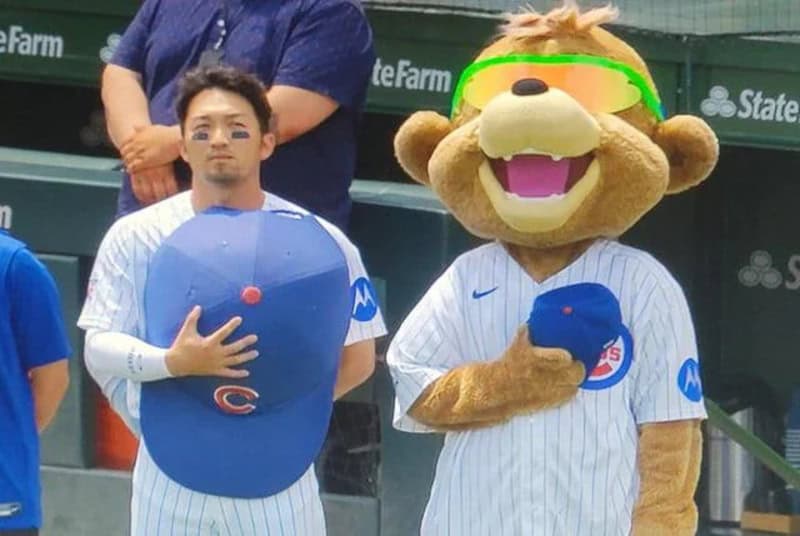 Person and mascot in baseball uniforms at a game, mascot wearing sunglasses.