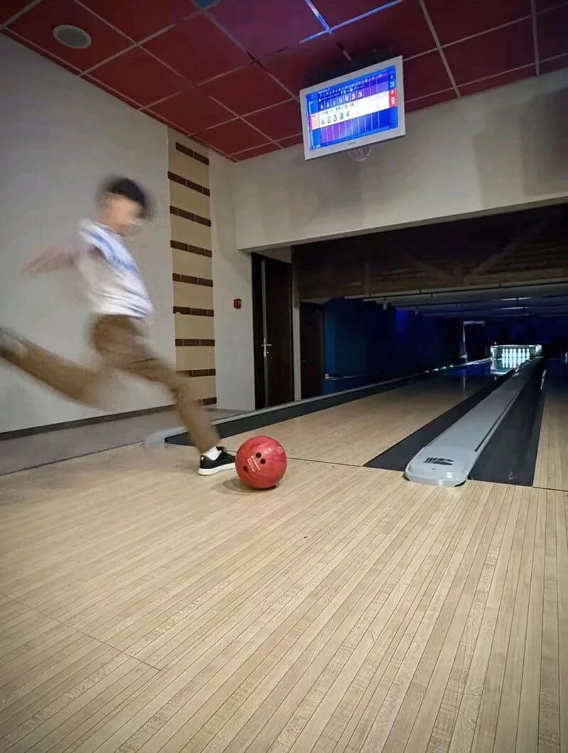 Child in bowling alley about to roll a red bowling ball down the lane.