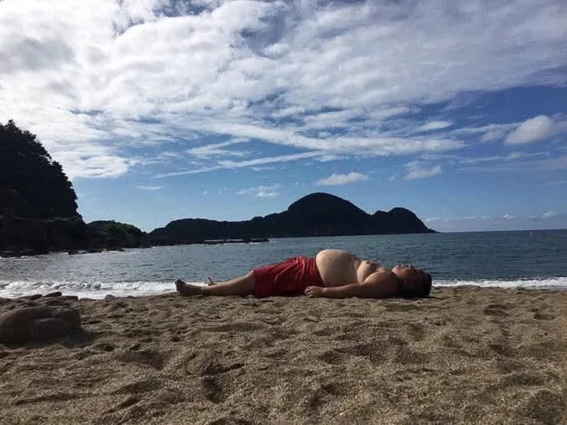 Person lying on the beach with a mountain and cloudy sky in the background.