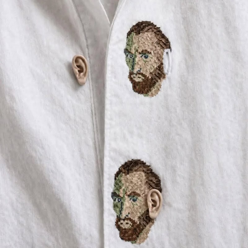 Two embroidered faces on a white shirt, with real ears attached below each face.