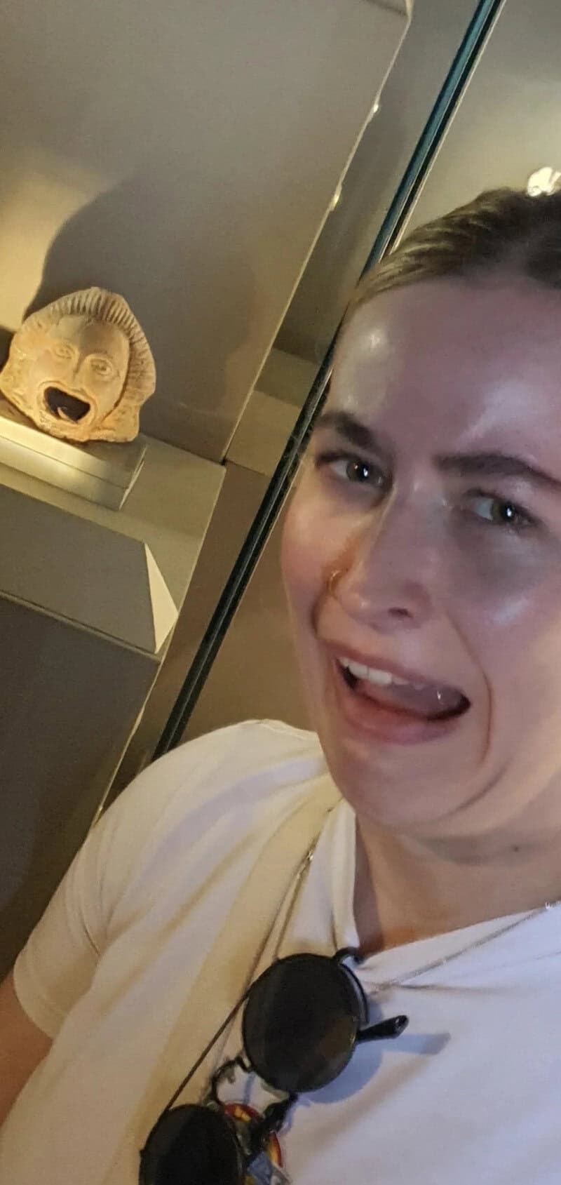 Person making a funny face with a mirror and a mask of a dog's face in the background.