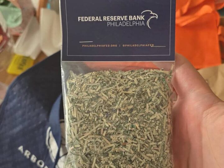 Hand holding a bag of dried herbs with a Federal Reserve Bank Philadelphia card on top.