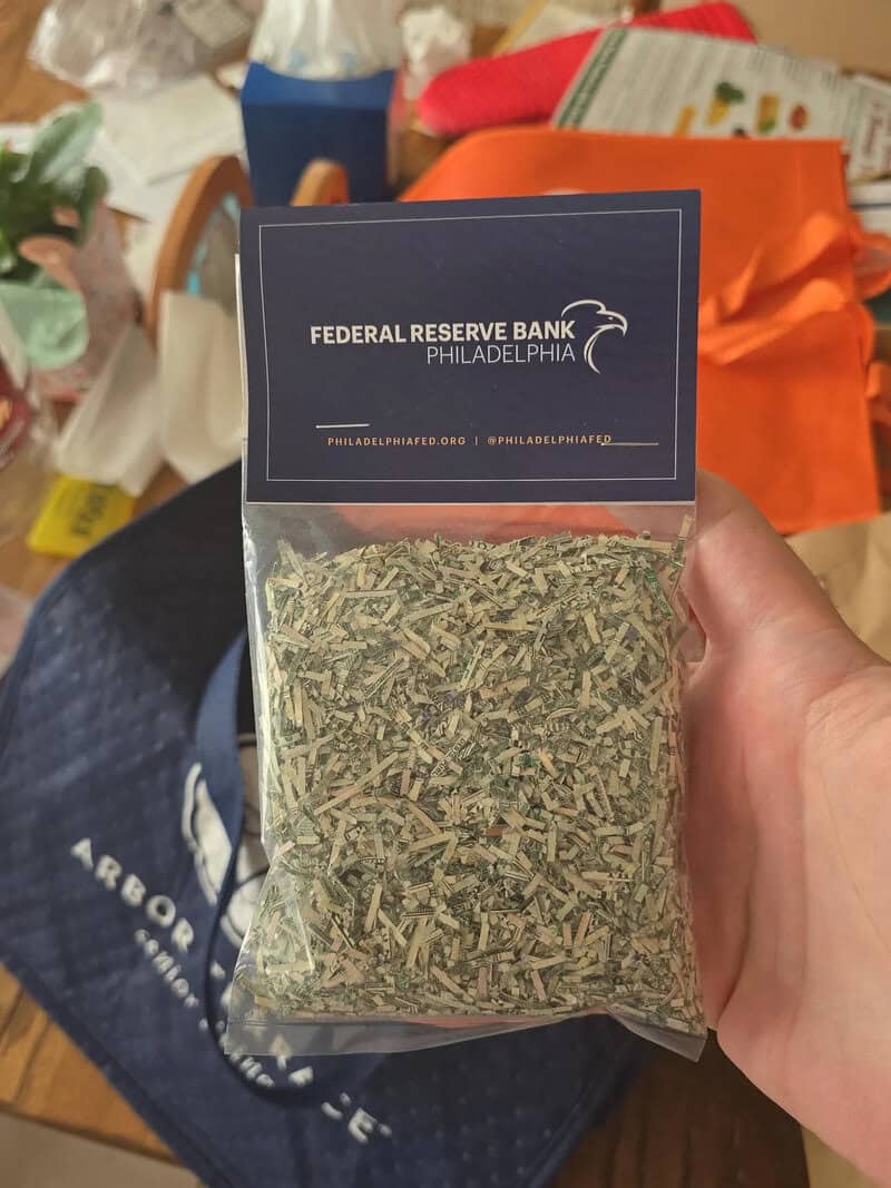 Hand holding a bag of dried herbs with a Federal Reserve Bank Philadelphia card on top.