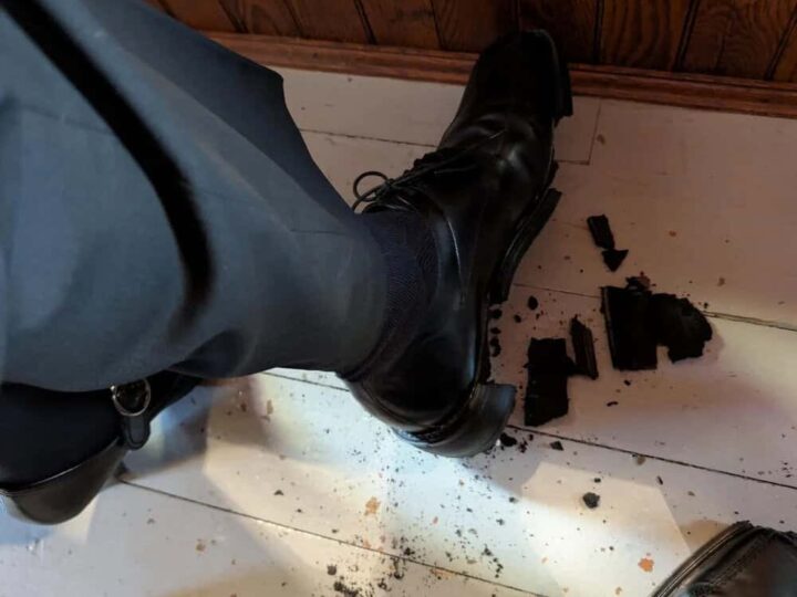 Person's foot in a black boot stepping on broken chocolate cookies on the floor.