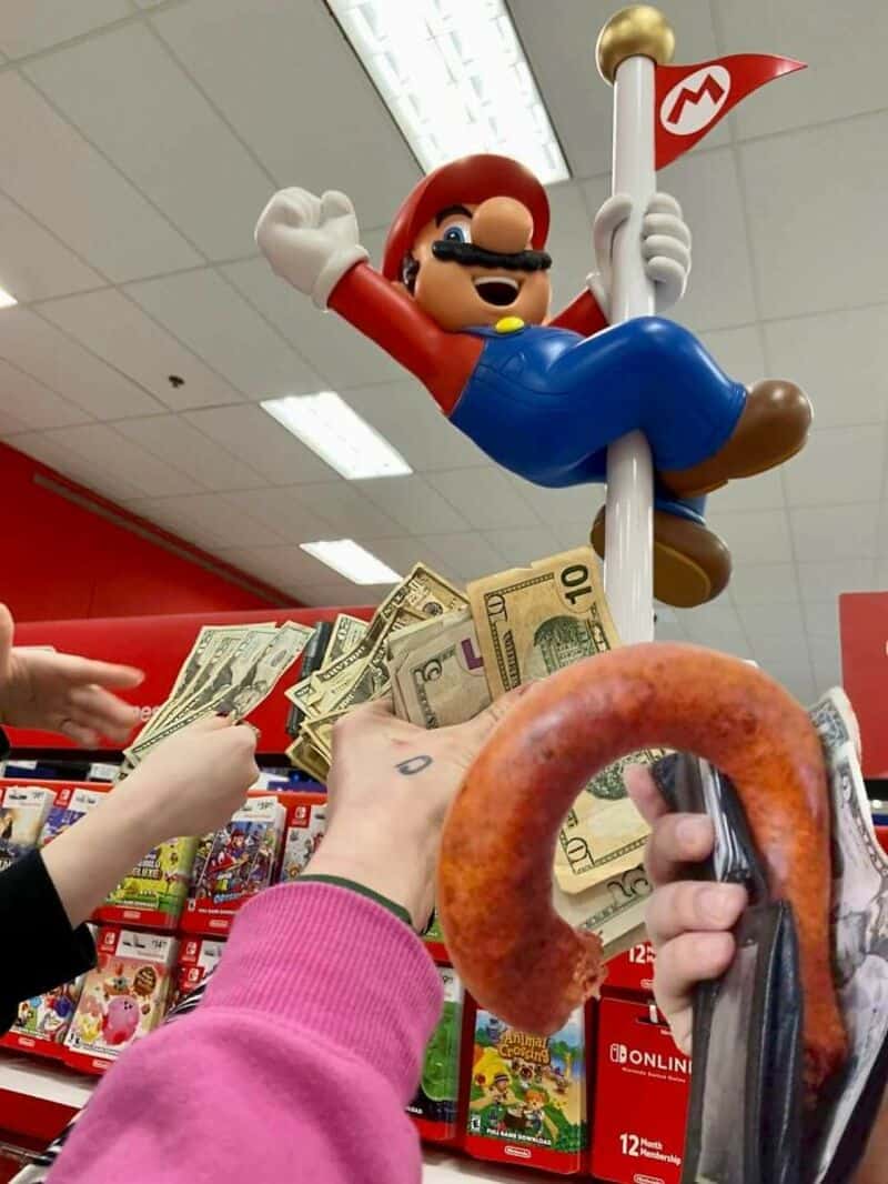 Mario statue holding a flag with money and a croissant in the foreground.
