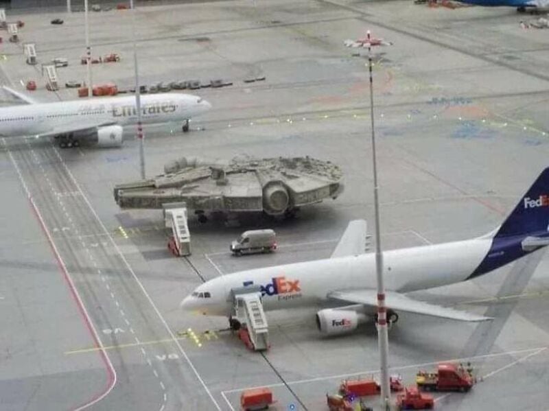 Tank on airport tarmac with FedEx plane and Emirates plane in background.
