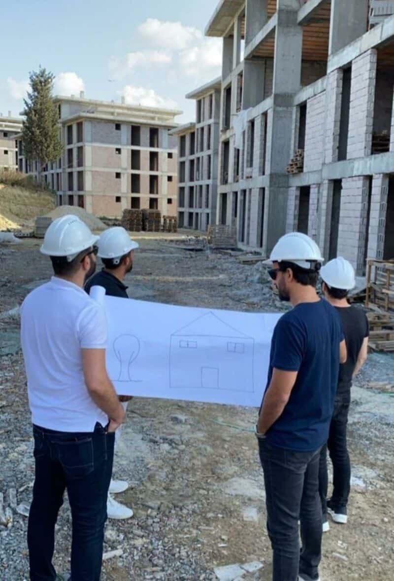 Group of four men in hard hats reviewing a blueprint at a construction site.
