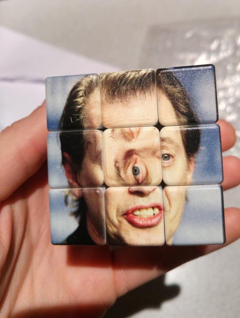 Hand holding a 3x3 puzzle cube with a distorted face image.