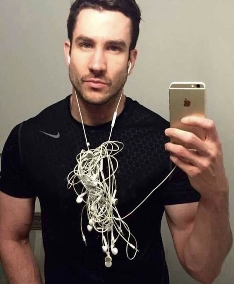 Man taking a mirror selfie with tangled earphones hanging around his neck.