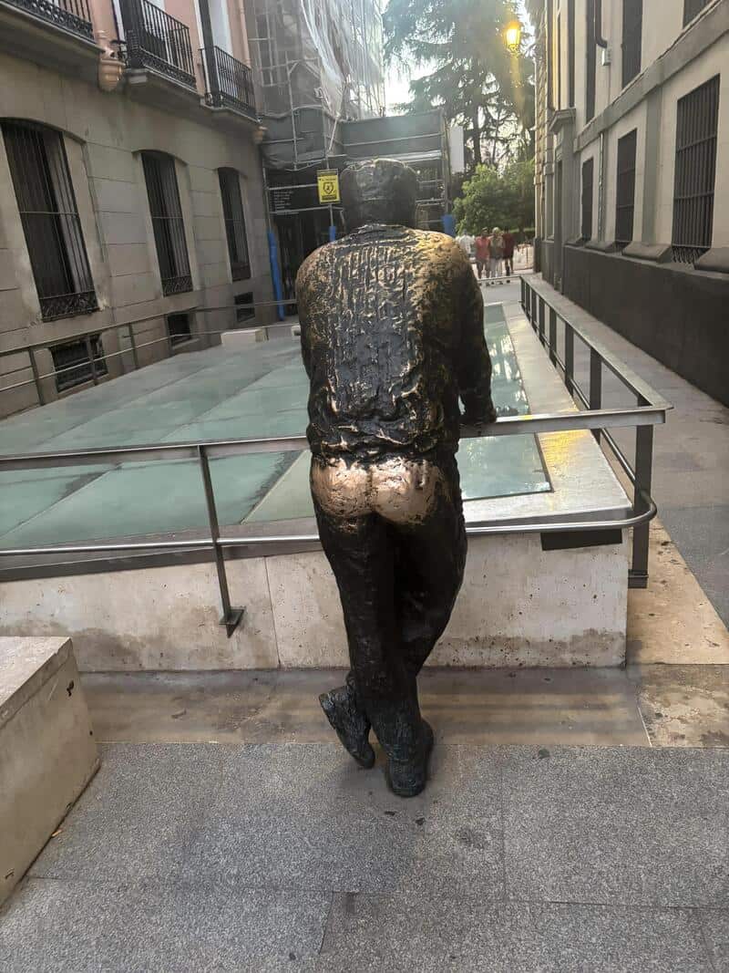 Bronze statue of a man leaning on a railing in an urban setting.