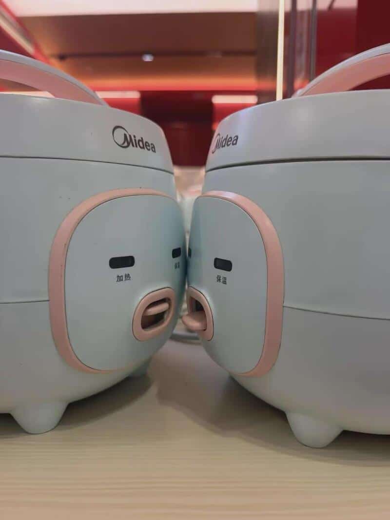 Two Midea rice cookers facing each other on a table.