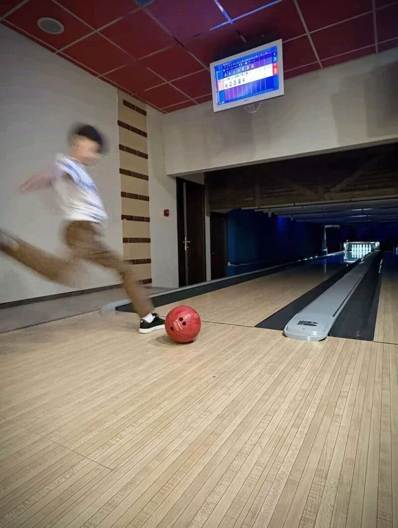 Child playing bowling with a red ball in an indoor alley.