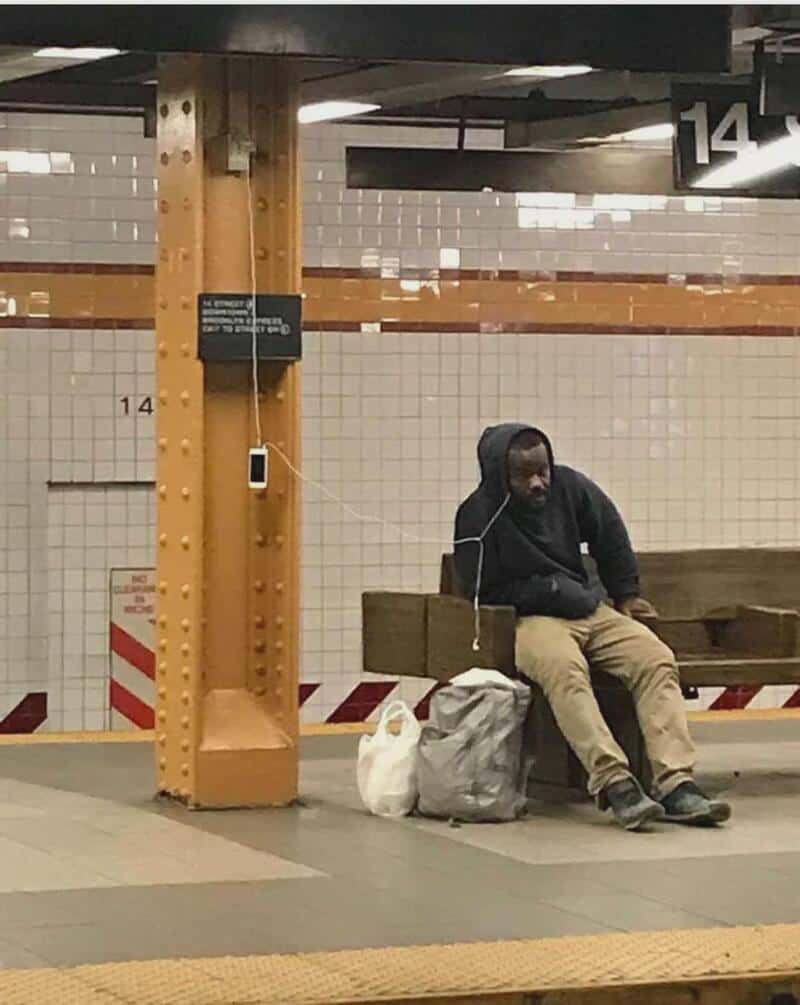 Man sitting alone on a bench in a subway station with bags beside him.