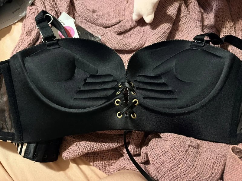 Black bra with lace-up front and adjustable straps on a pink textured fabric.