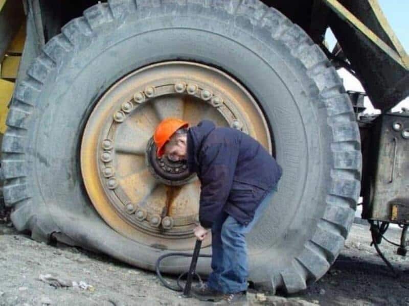 Man inspecting a large tire of a heavy-duty vehicle with a tool.