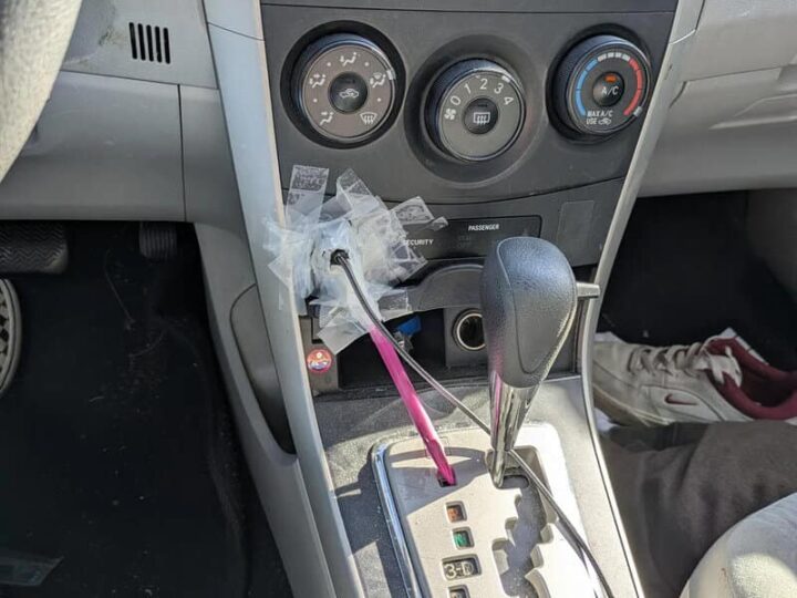 Car interior with gear shift, climate controls, and a plastic bag with a pink stick inside.
