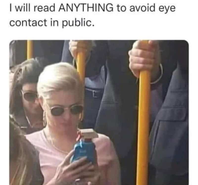 Person with short blonde hair and sunglasses looking at phone, surrounded by others holding yellow t.