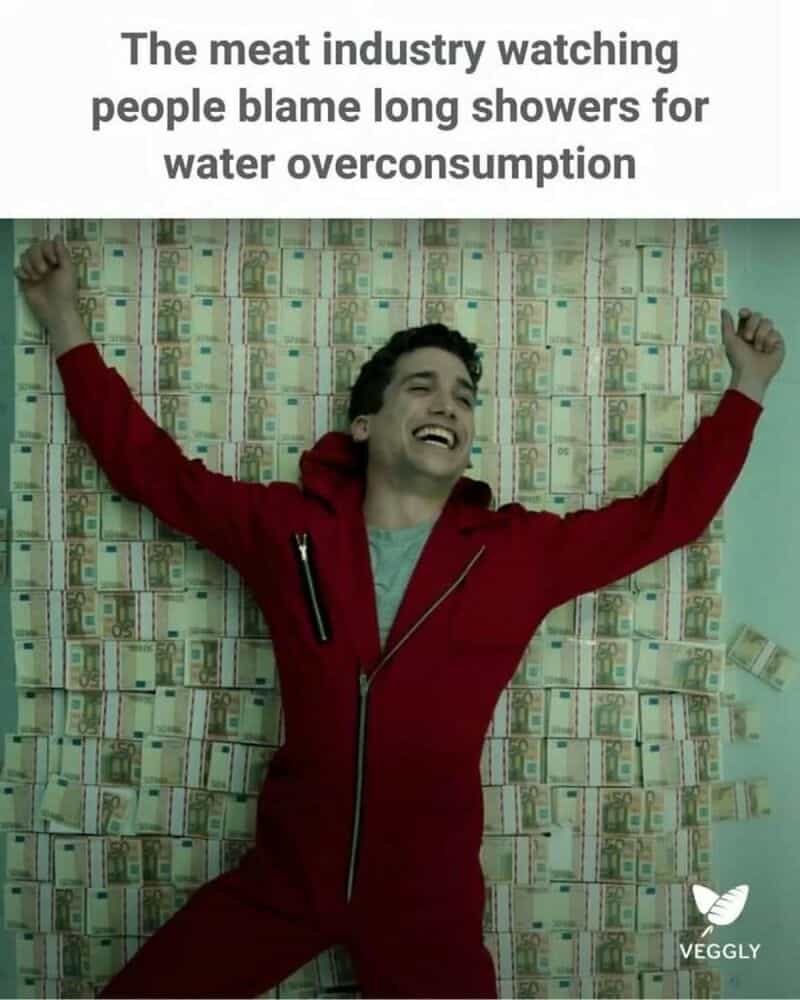 Man lying on floor covered with dollar bills, smiling with arms raised.