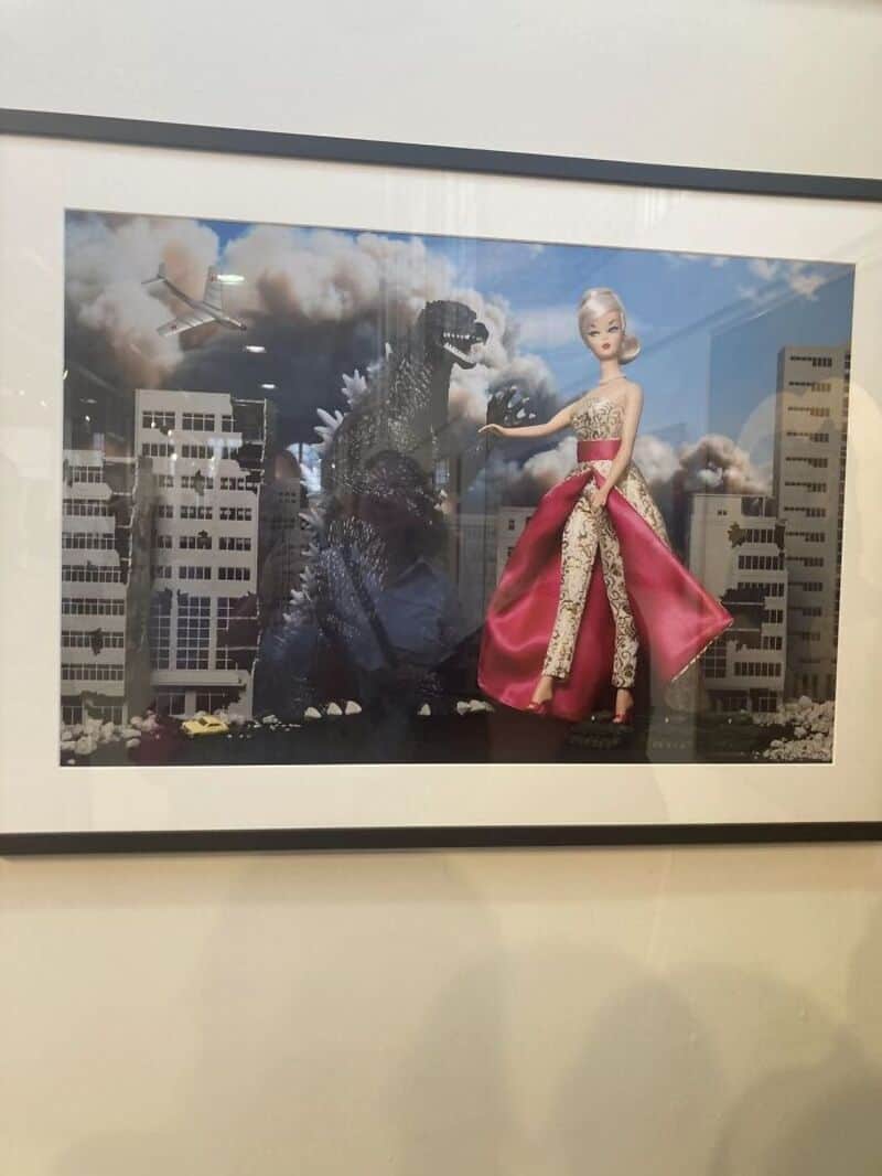 A giant doll in a pink dress fights a Godzilla-like monster in a cityscape.