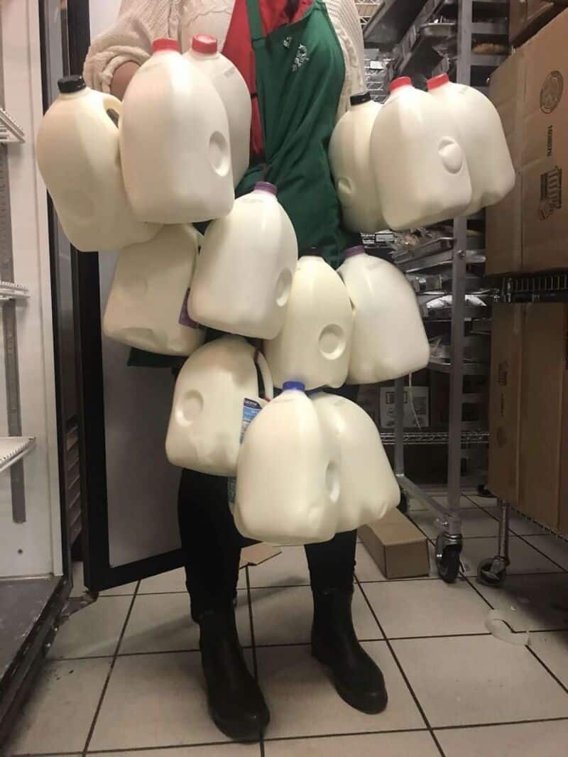 Person with multiple large white jugs hanging from their body in a storage room.