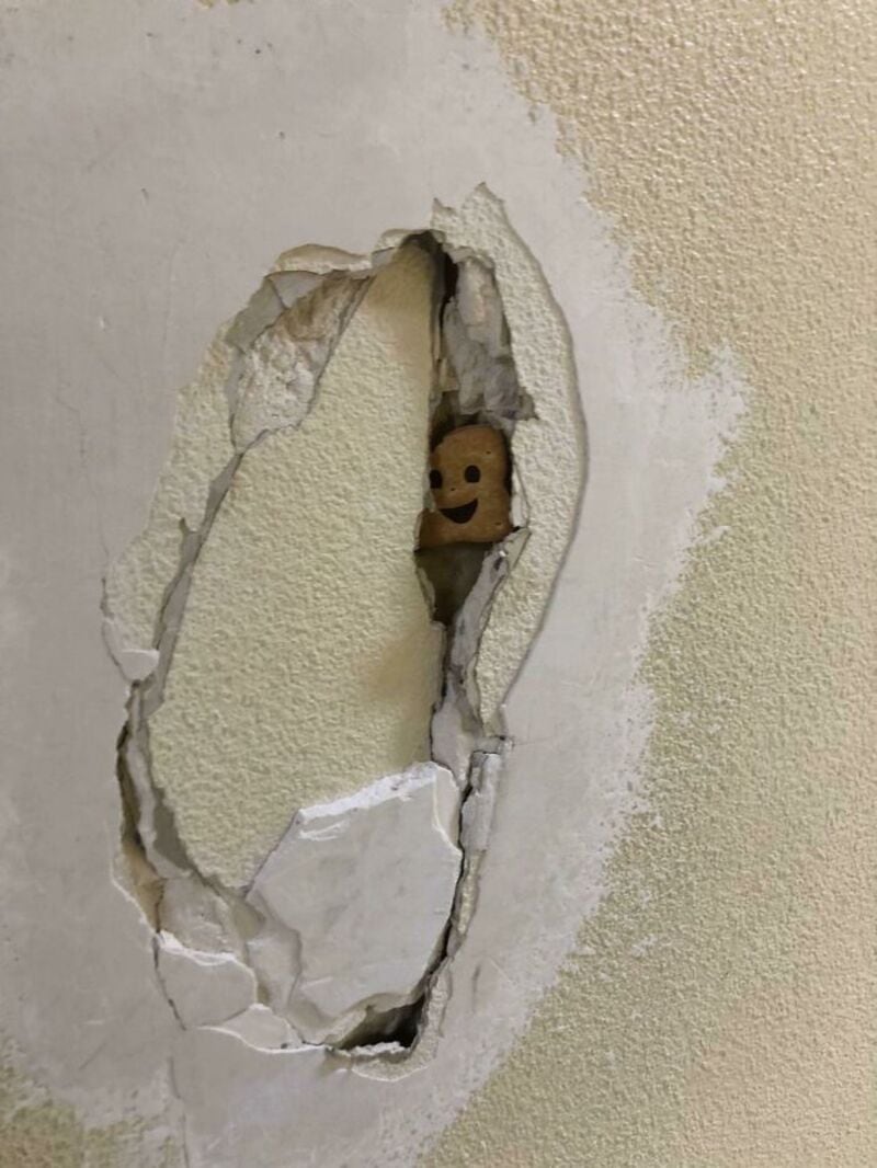 A small smiling face peeking through a hole in the wall.