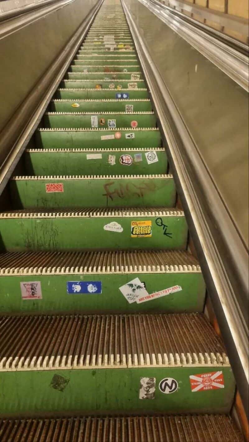 Green escalator with various stickers and graffiti, no people present.