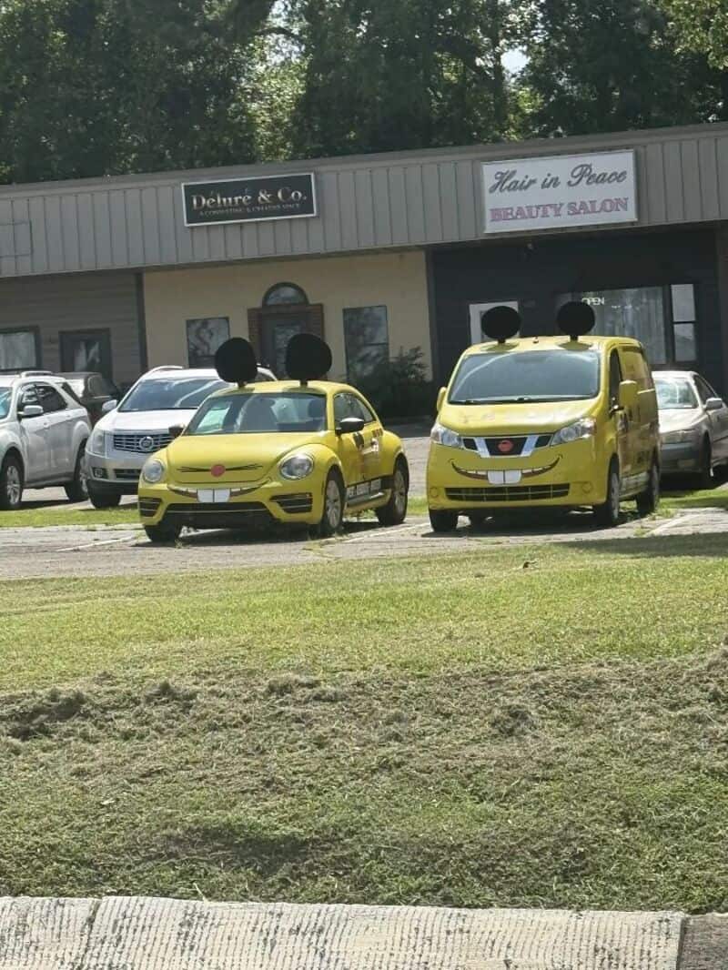 Two yellow cars with black circles on top, parked in front of a building.