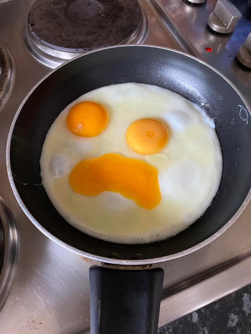Three eggs in a frying pan, one with a yolk shaped like a smiley face.