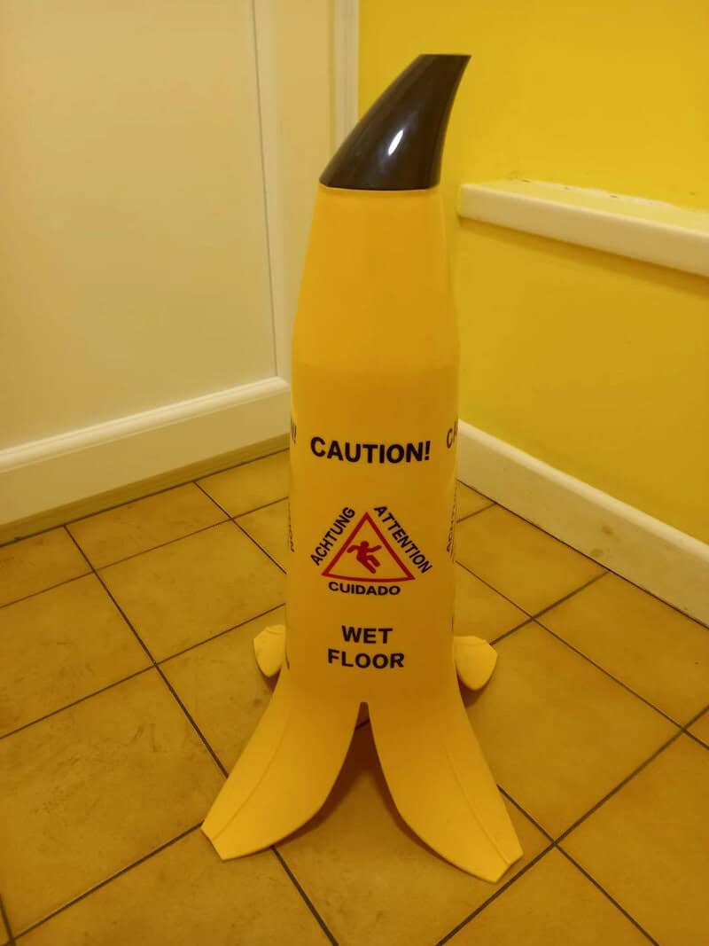 Banana-shaped wet floor sign with caution labels in a yellow room.