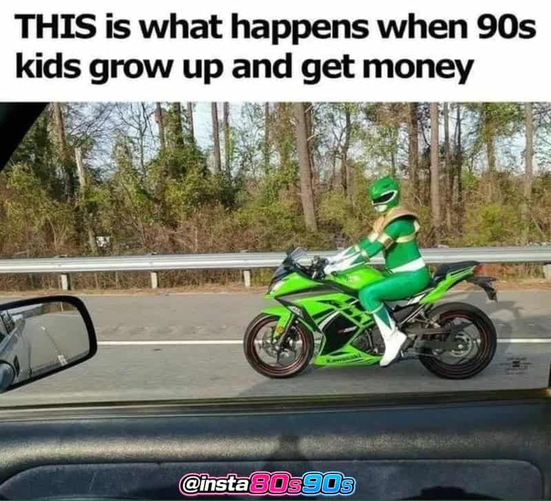 A person in a Power Rangers costume riding a green motorcycle on the road.