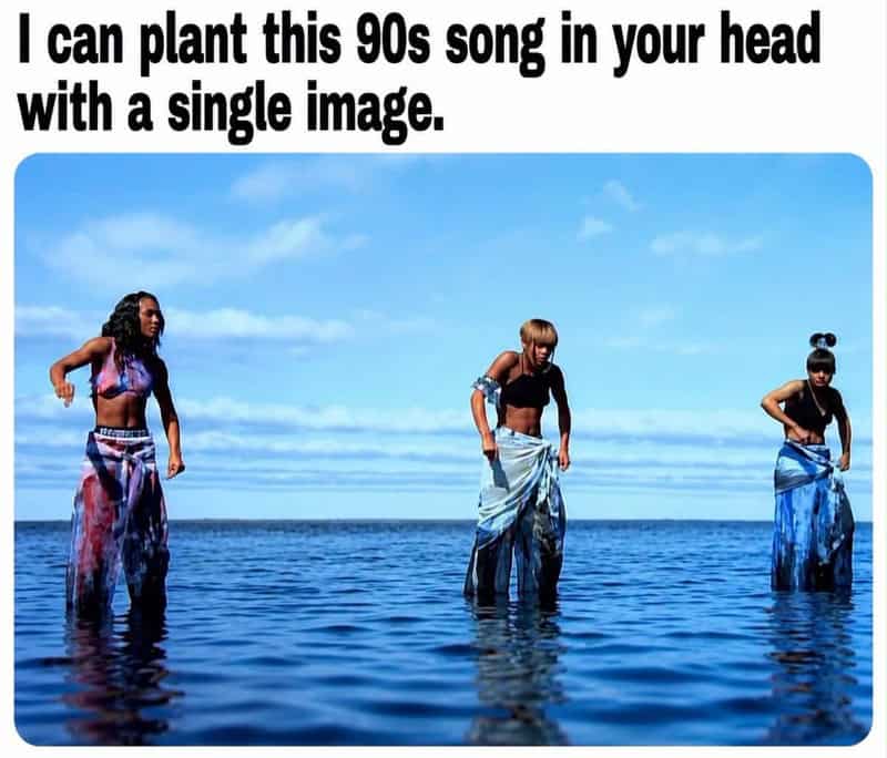 Three women standing in water with pants pulled up, under a blue sky.