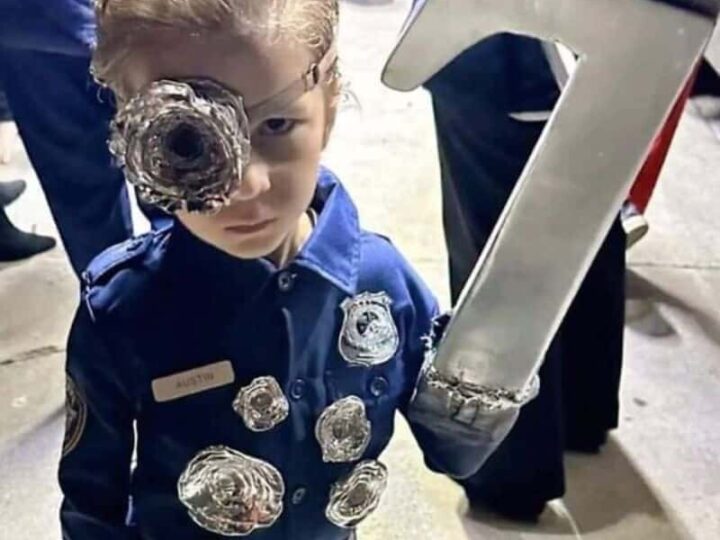 Child in police uniform with a makeshift eye patch and a large metal object on the face.