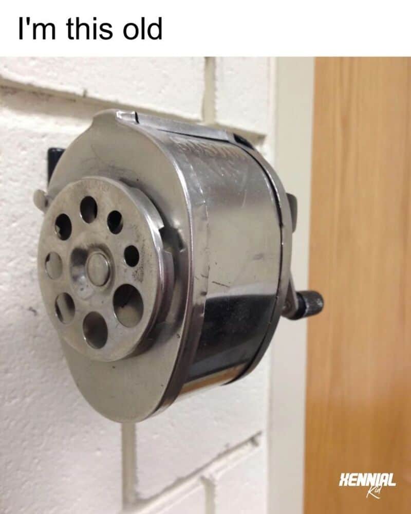Old metal pencil sharpener mounted on a white brick wall with text 'I'm this old'.
