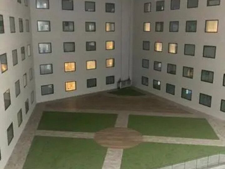 Interior view of a courtyard with green grass and pathways, surrounded by a building with many small.