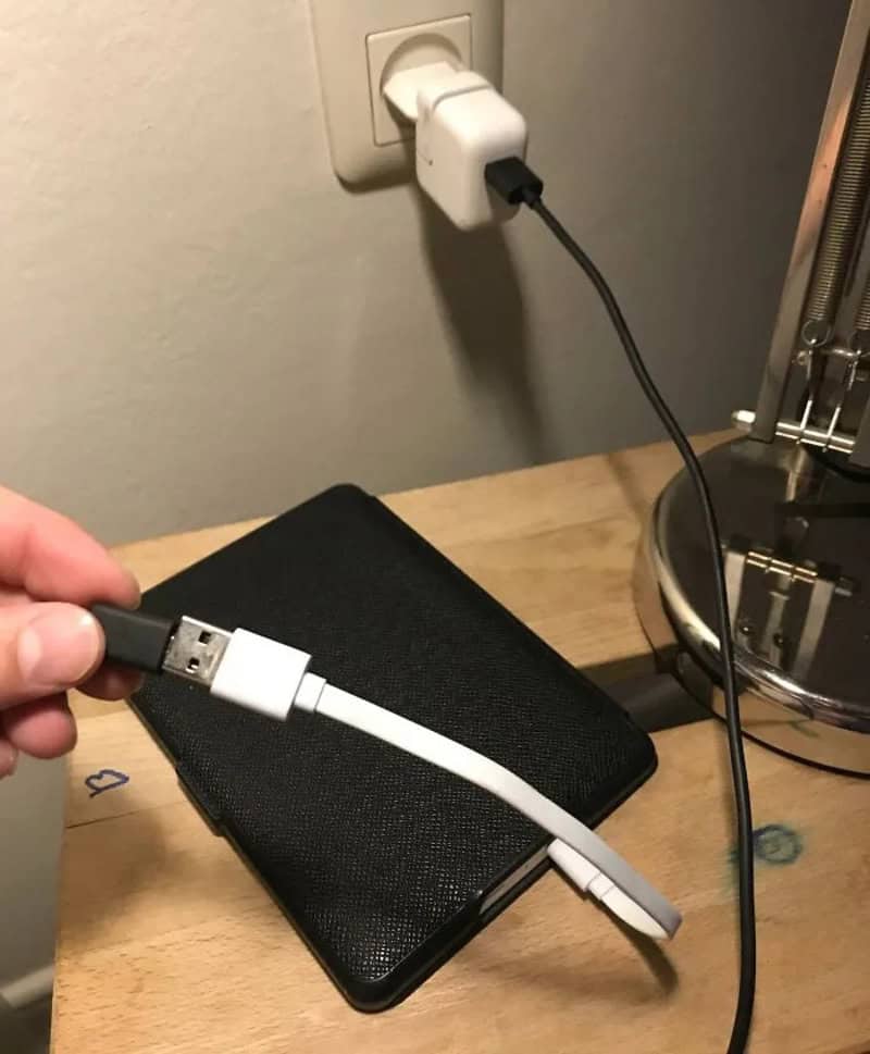 A hand holding a USB cable near a black device plugged into a wall socket.