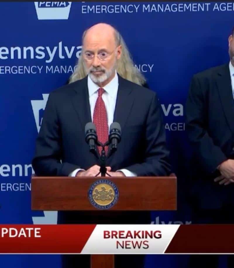 Man with long hair and beard speaking at a podium during a press conference.