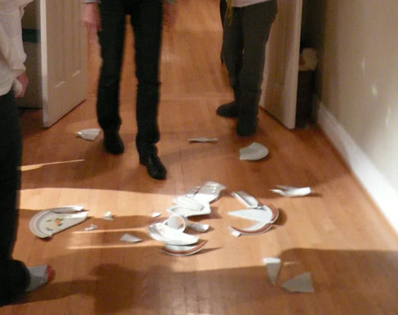 Broken plates on the floor with two people standing nearby.