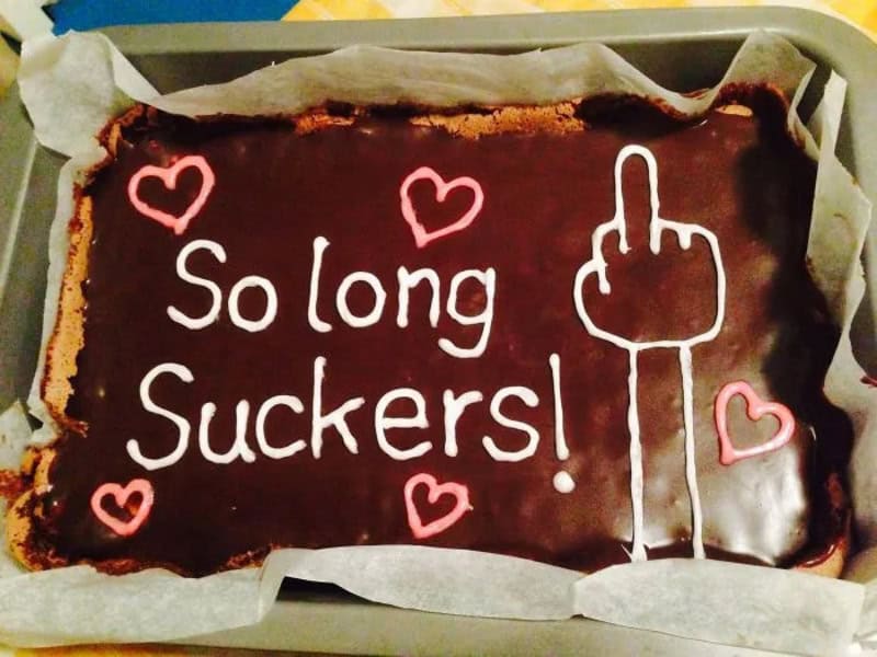 Chocolate cake with pink hearts and a middle finger drawing, saying 'So long Suckers!'.