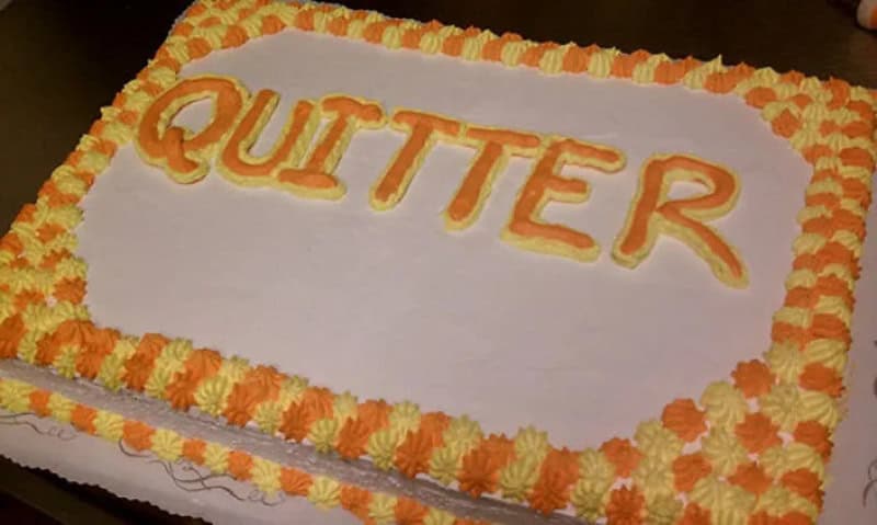 Cake with 'QUITTER' written in orange and yellow icing, decorated with orange and yellow flowers.