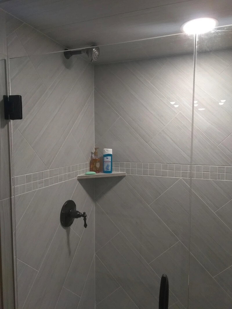 Shower with a shelf holding toiletries, light fixture, and a shower head.