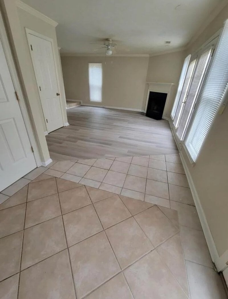 Empty room with mismatched tile and wood flooring, fireplace, and large windows.