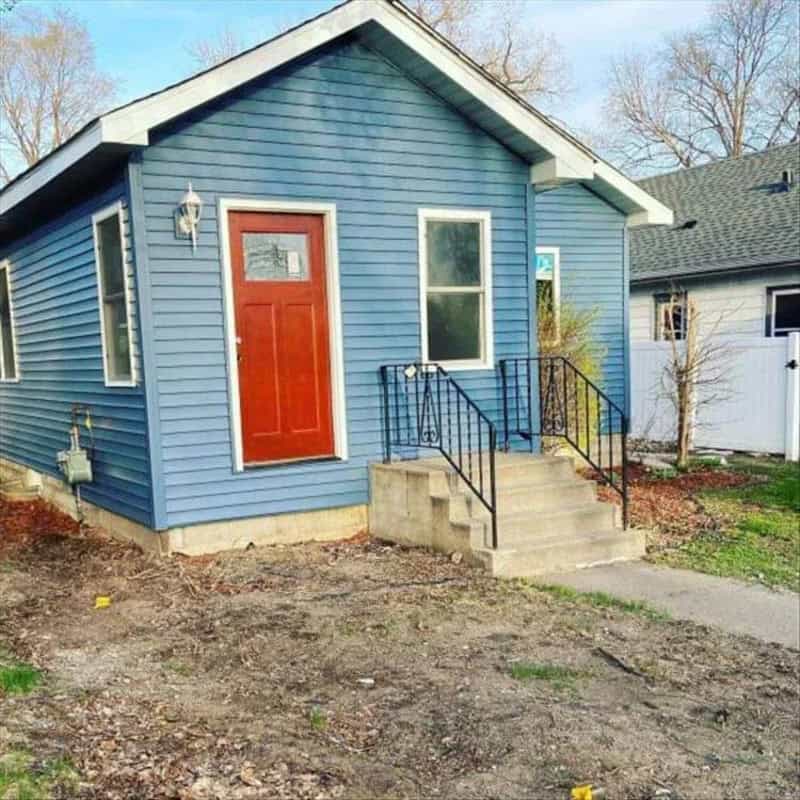 Blue house with red door and stairs, under a clear sky.