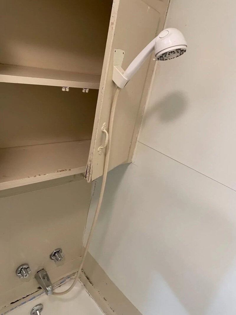 Shower head attached to a cabinet door in a bathroom.