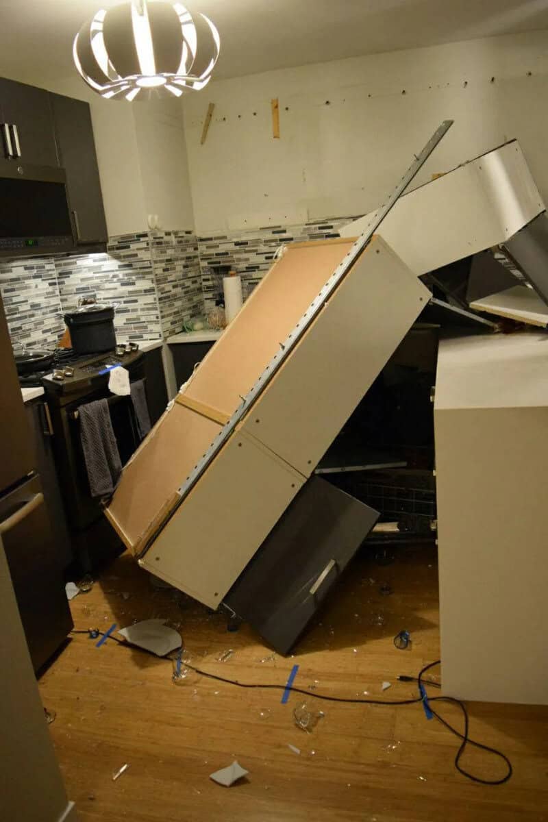 A toppled refrigerator in a kitchen with a damaged wall and scattered debris.