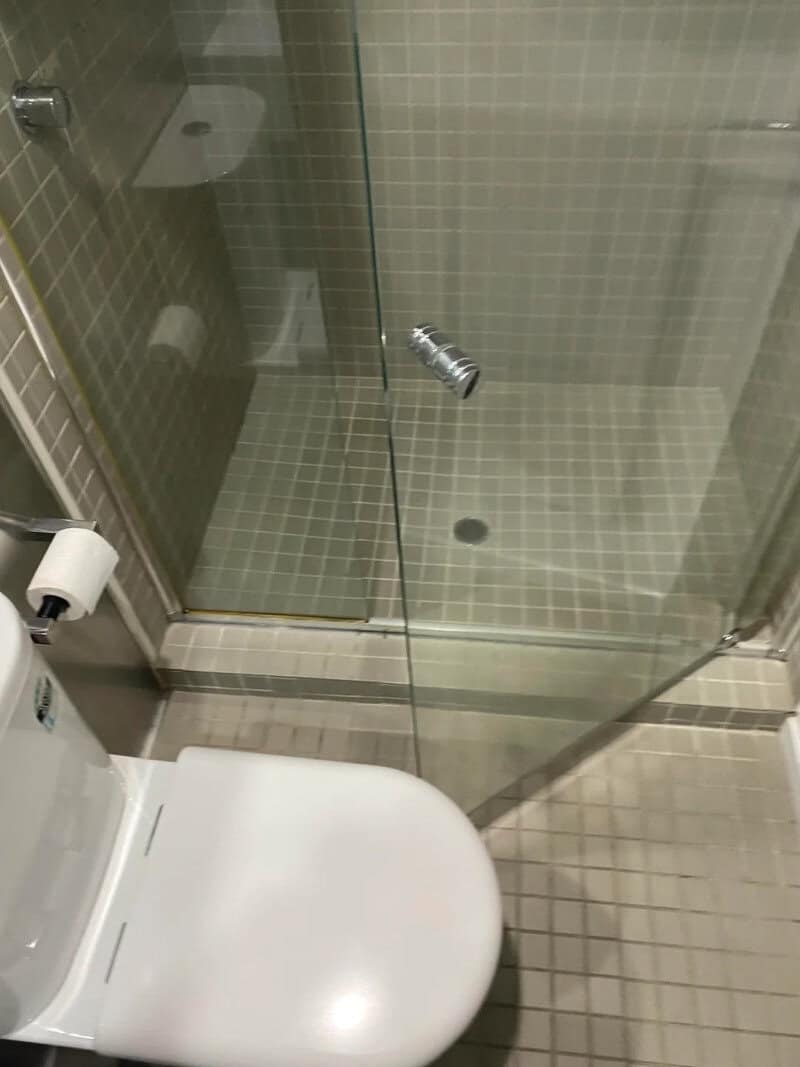Shower head installed inside a toilet room with a glass door and tiled walls.