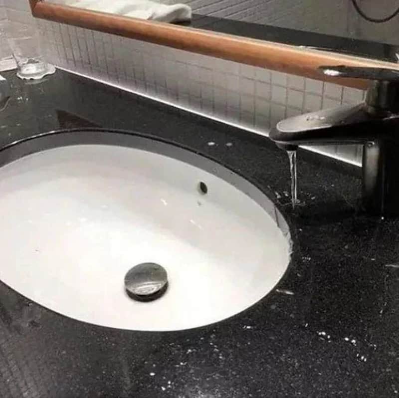 Sinking sink with a bent faucet and a coin in the basin.